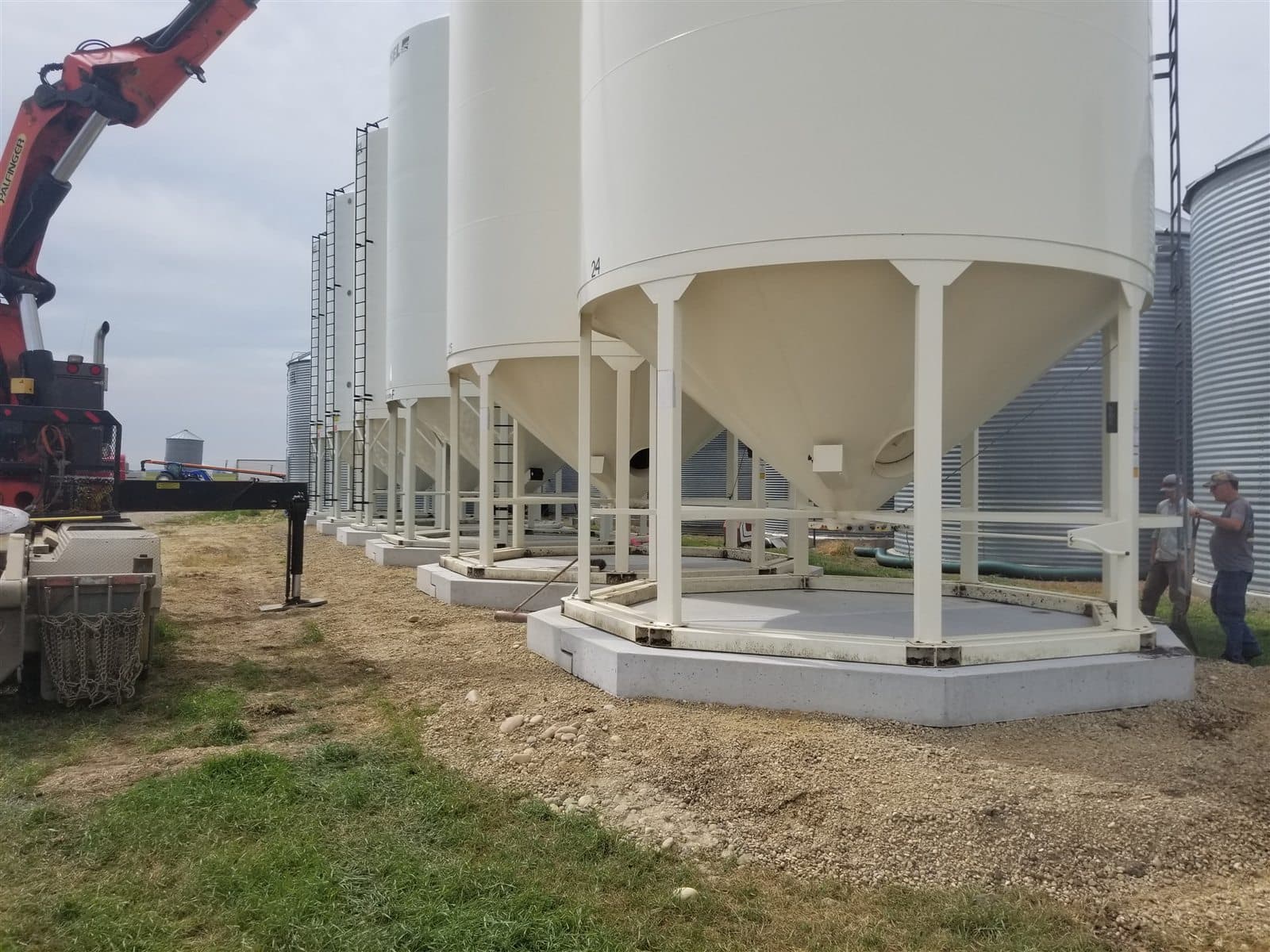 AltaMix precast bin pads supporting a row of hopper grain bins on a farm.